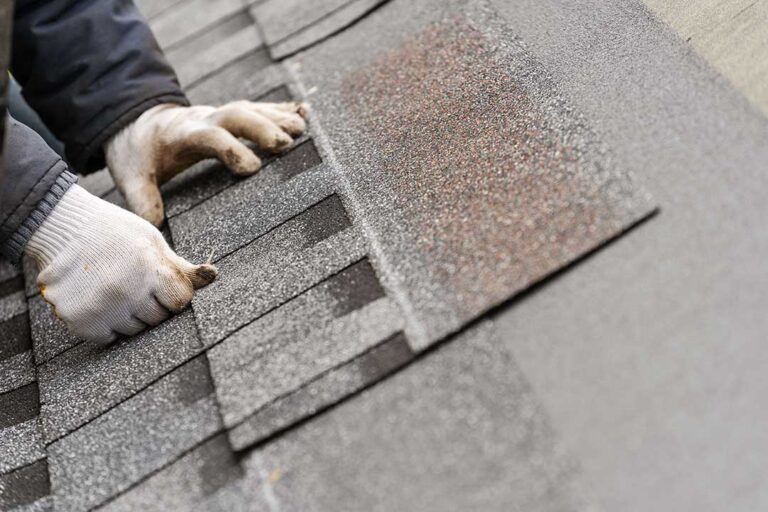 A close-up of a residential roof with faded shingles and visible storm debris on the surface.